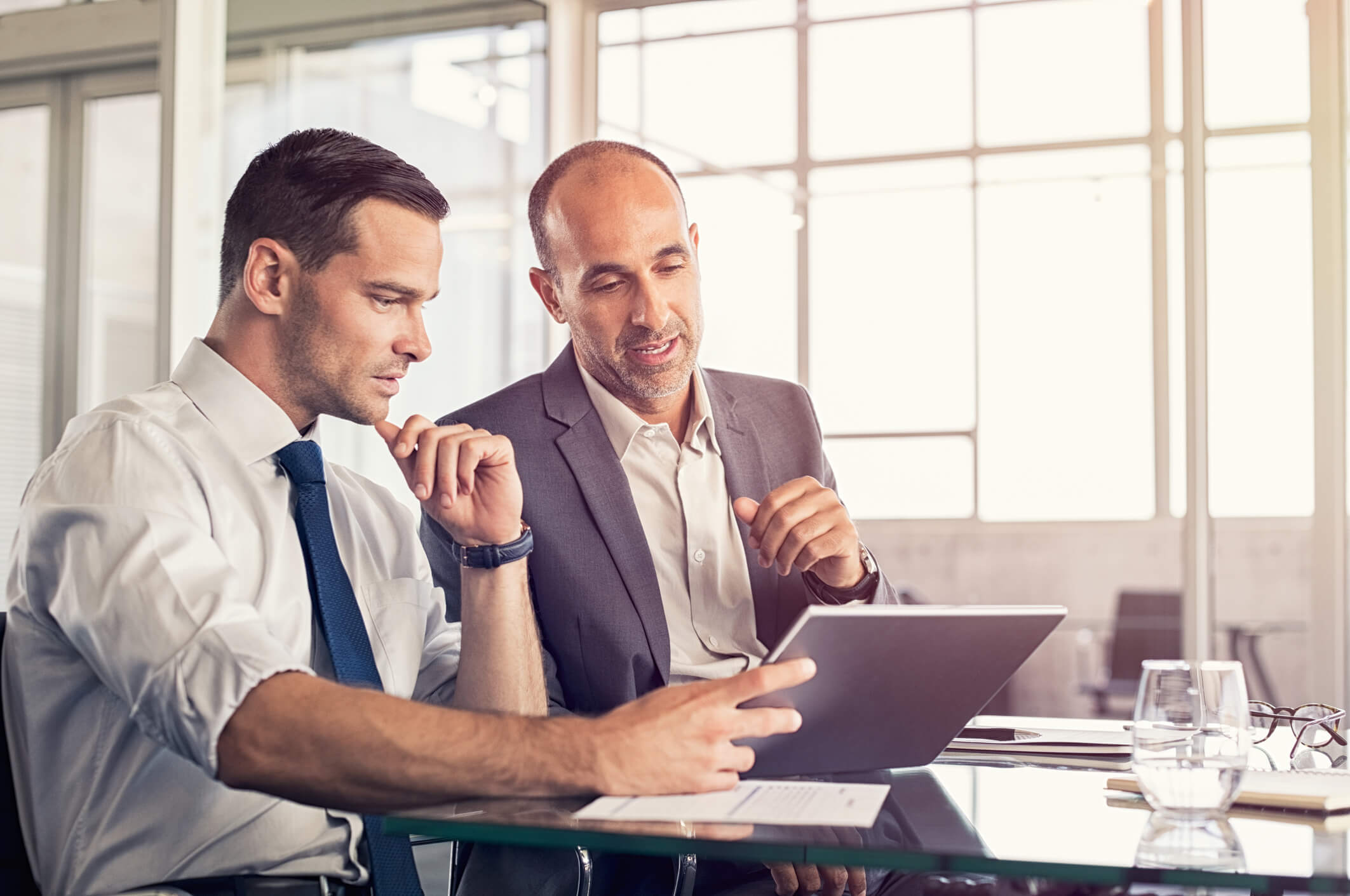 Two men sat at desk in office looking at tablet
