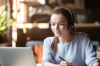 Focused woman wearing headphones using laptop in cafe, writing notes, attractive female student learning language, watching online webinar, listening audio course, e-learning education concept