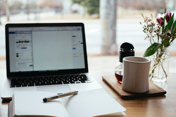 Laptop, notebook, coffee mug and flowers in vase on table