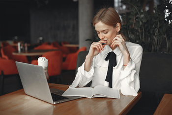 Woman sat at table reading notes in front of laptop 