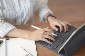 Person typing on laptop with pen in hand