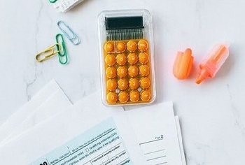 Calculator on desk next to paperwork, paper clips and highlighter pen